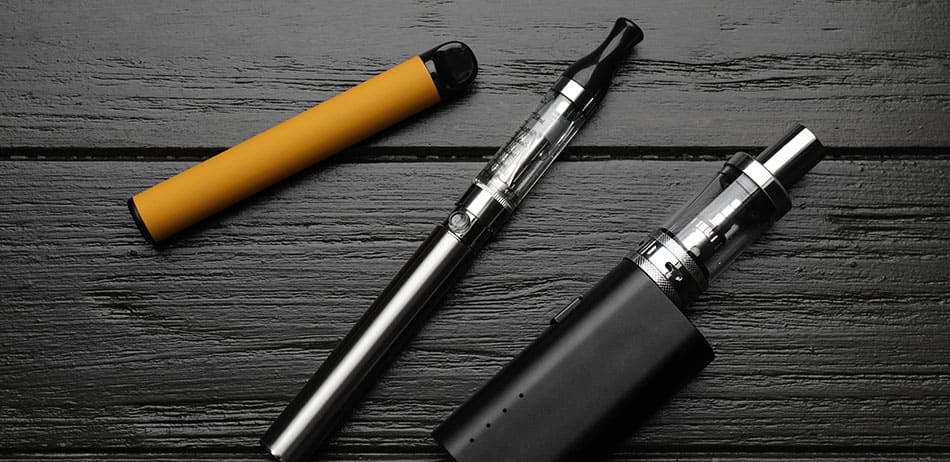 Collection of different vaping devices laid out on a black wooden background