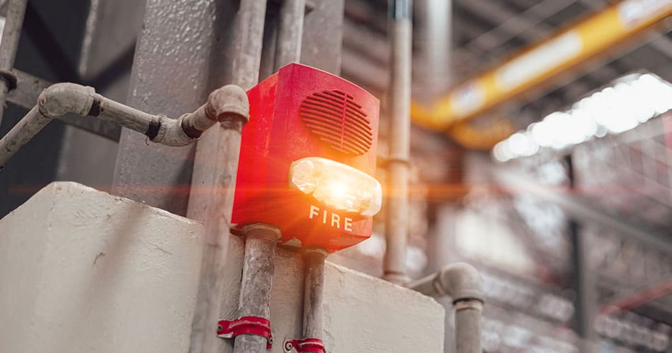 Fire alarm in a warehouse setting with light flashing red.