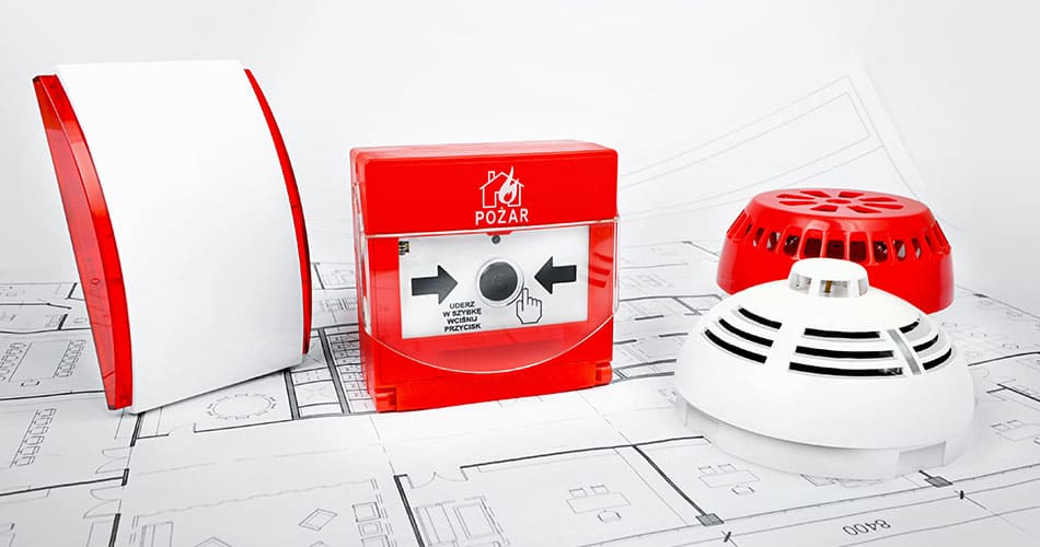 Fire alarm system laid on a table next to a red and white smoke alarm.