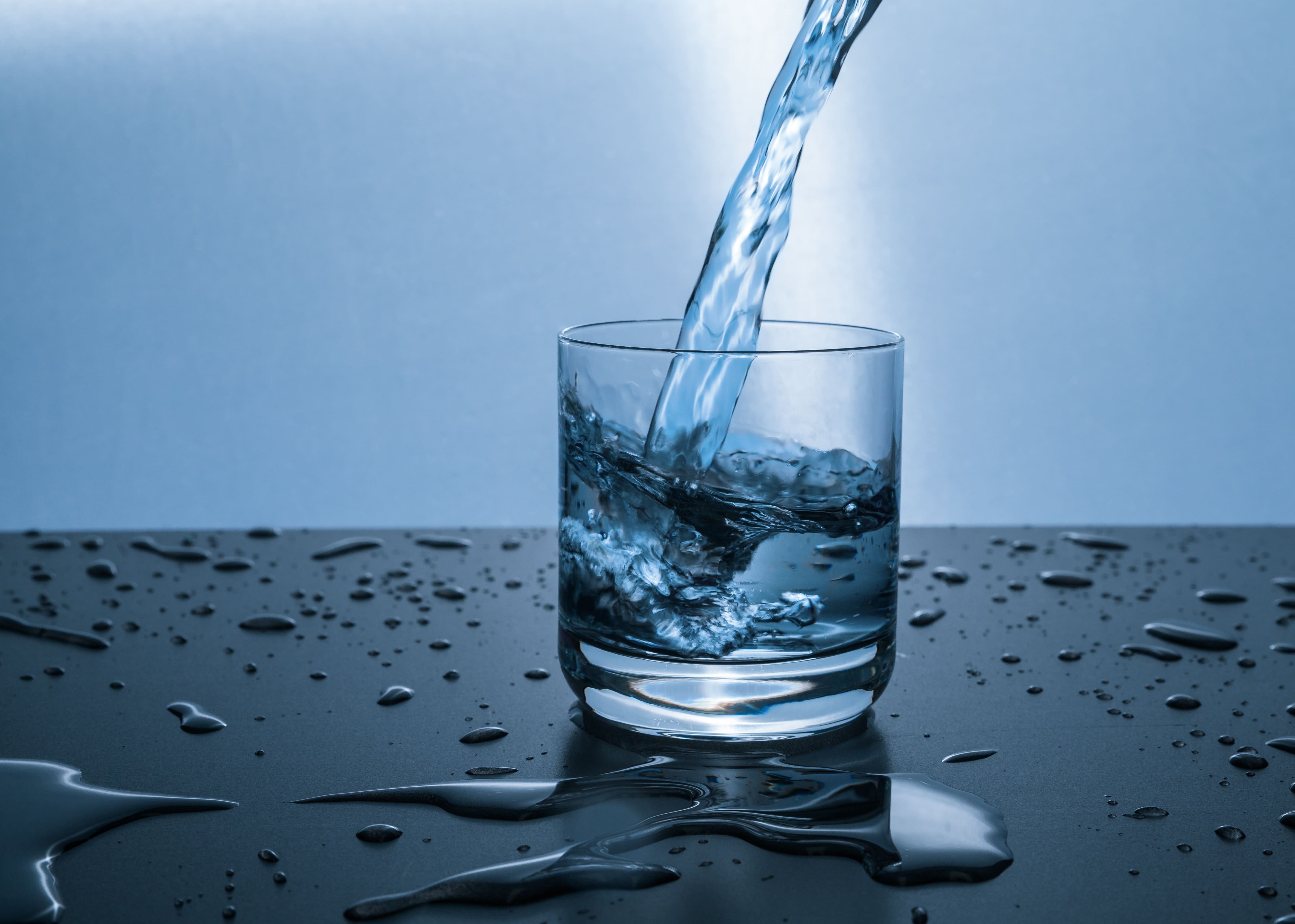 Glass of water being filled from above, with droplets of water surrounding the glass.