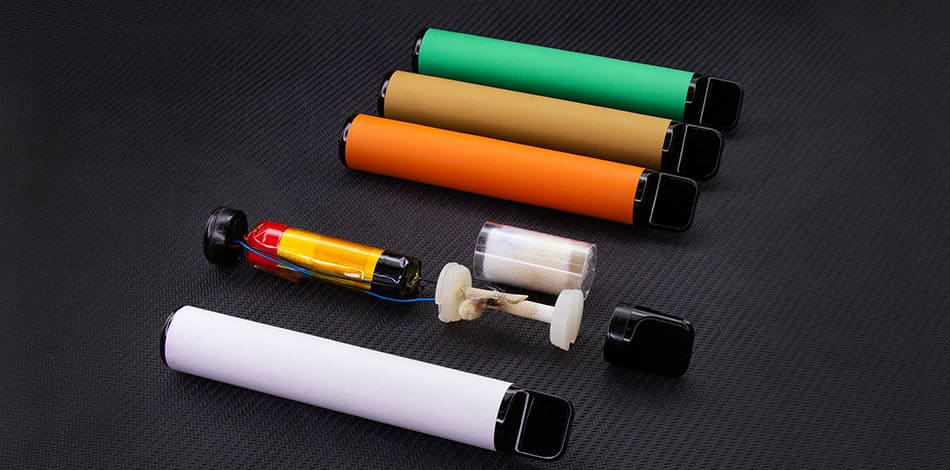 Row of disposable vape devices with one showing the internal battery and components within