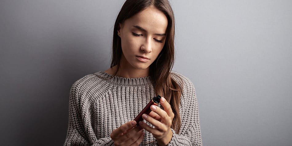 Woman looking at disposable vape in her hands.