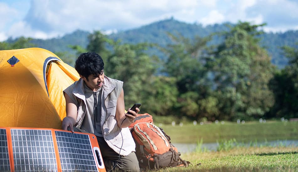 Man charging his phone next to tent in middle of a field.