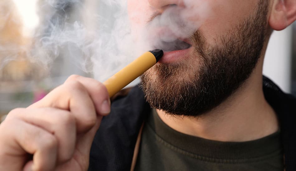 Close up of a man vaping on a disposable e-cigarette.