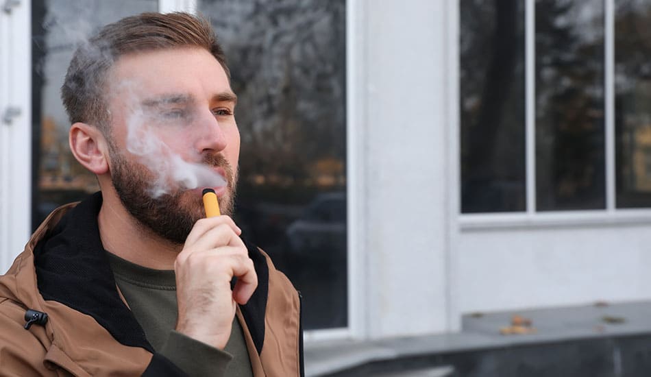 Man stood outside vaping orange disposable e-cigarette.