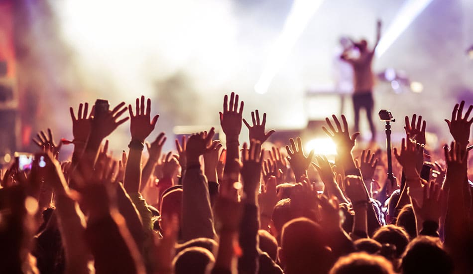 People with raised hands looking towards a band playing on stage at a music concert.