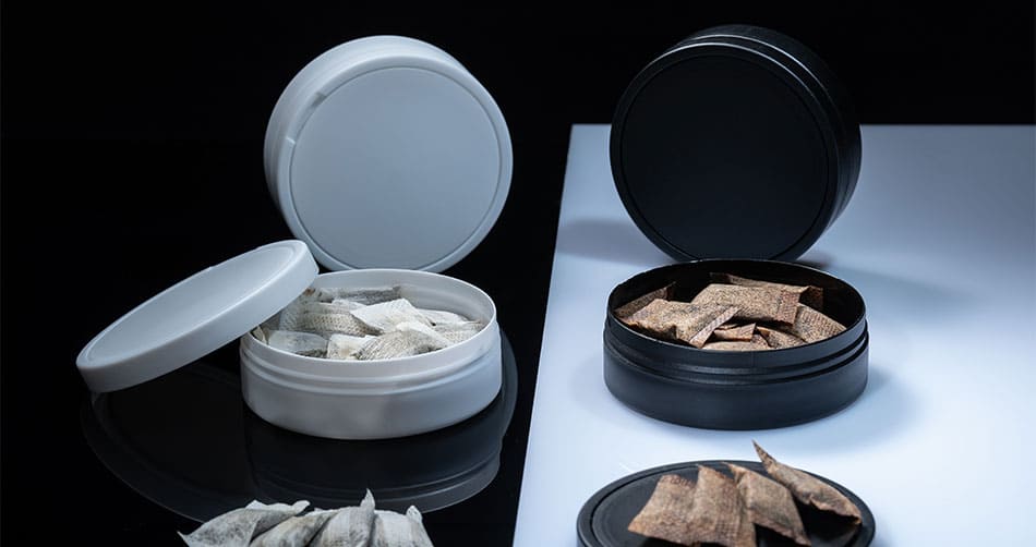 White and black tubs of nicotine pouches on a table with pouches taken out.