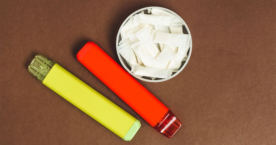 Two disposable vape devices on a table next to an open tub of nicotine pouches.