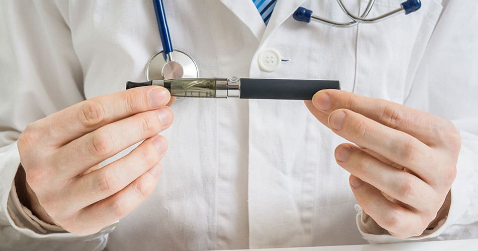 Person wearing white science lab coat holding an e-cigarette between their hands looking close at the device.