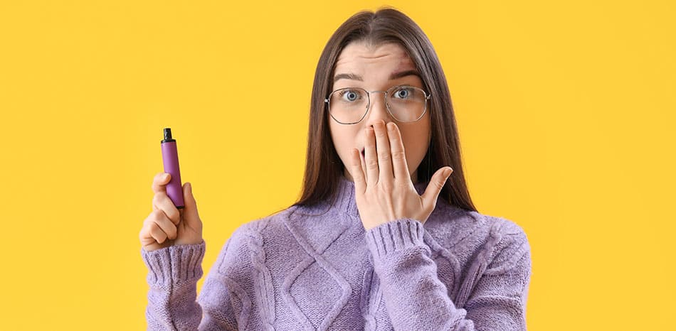 Woman looking shocked with hand over her mouth and the other hand holding a disposable vape