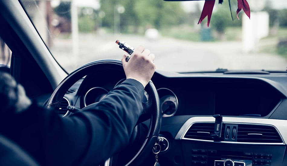 Person driving whilst holding the wheel with a vape kit in their hand.