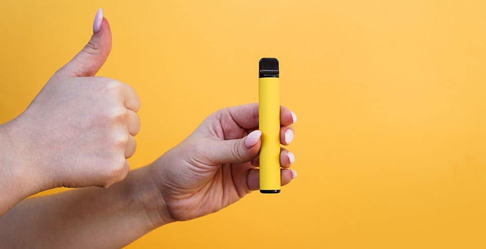 A disposable vape in one hand with the other hand showing a thumbs up