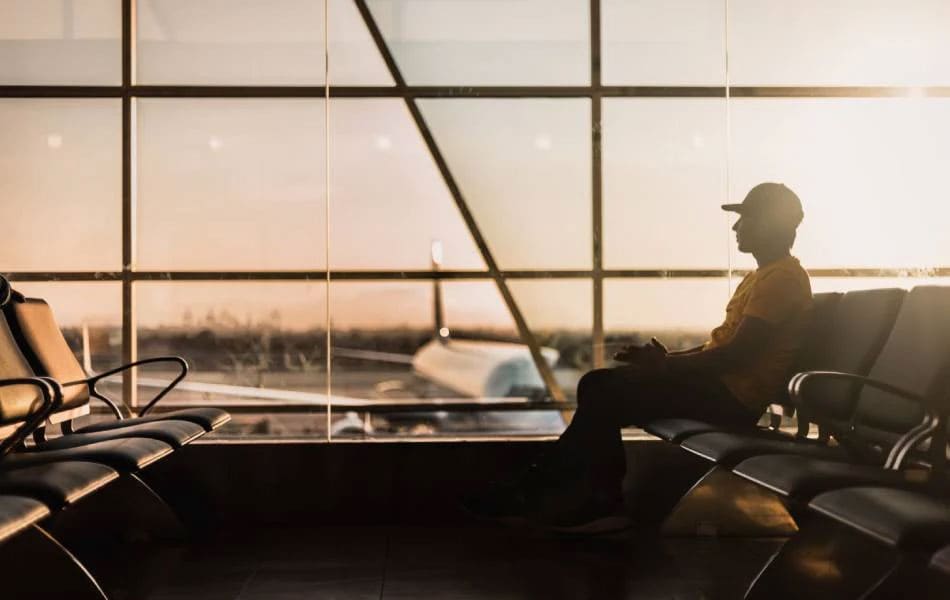 Person sat on a bench in an airport looking out through a large glass window at a plane parked on the runway.