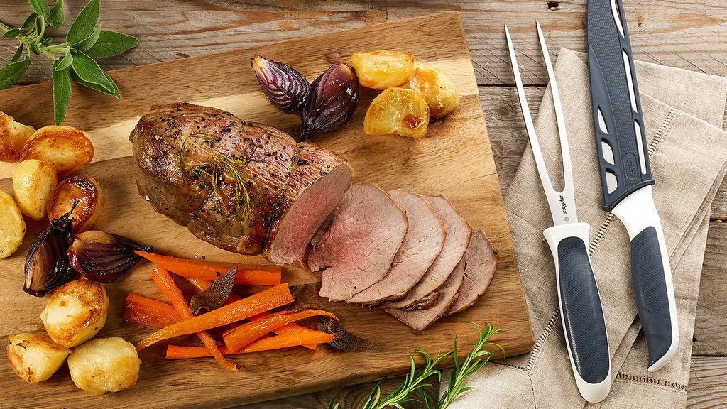 carving knife and fork next to a cut of beef and roast vegetables