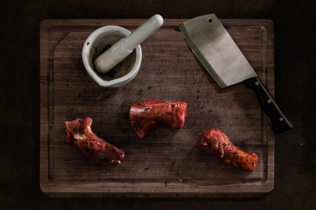 cleaver with cut meat and pestle and mortar on wooden chopping board