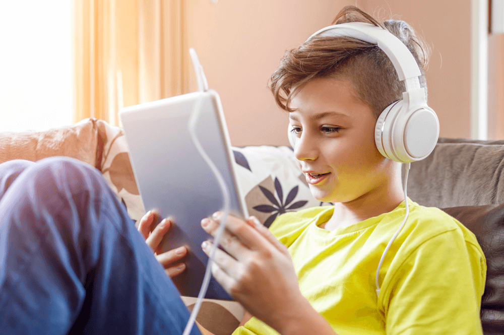 Child in a yellow shirt sitting on a couch wearing headphones and using a tablet