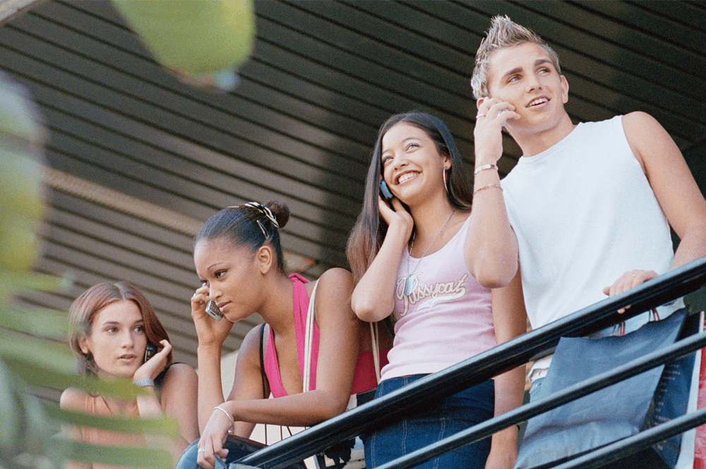 Four teenagers standing against a railing talking on cell phones.