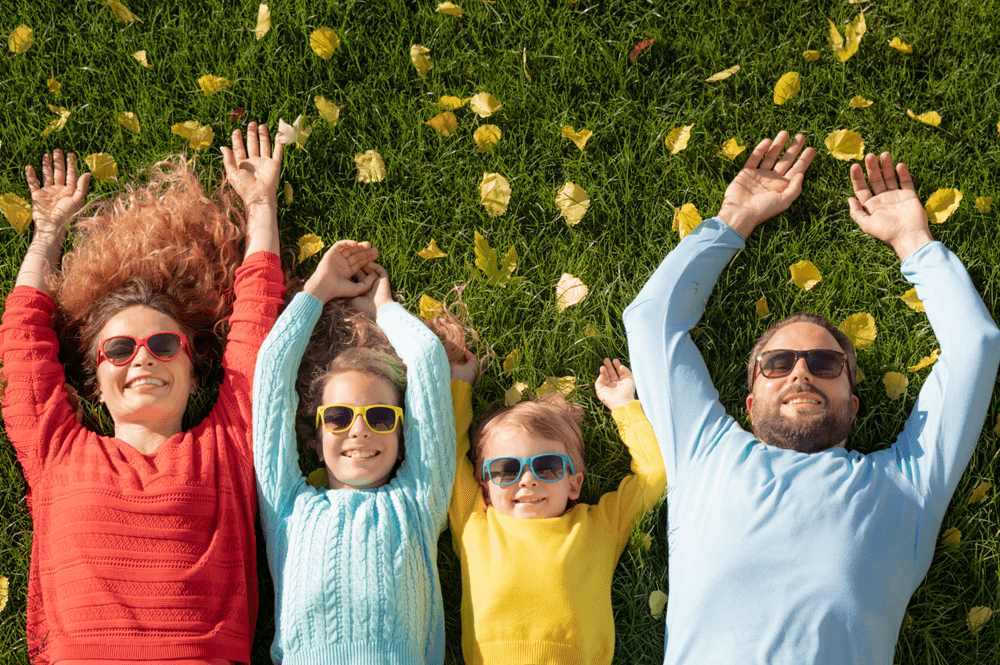 a family of four wearing sunglasses and laying in the grass with their arms above their heads