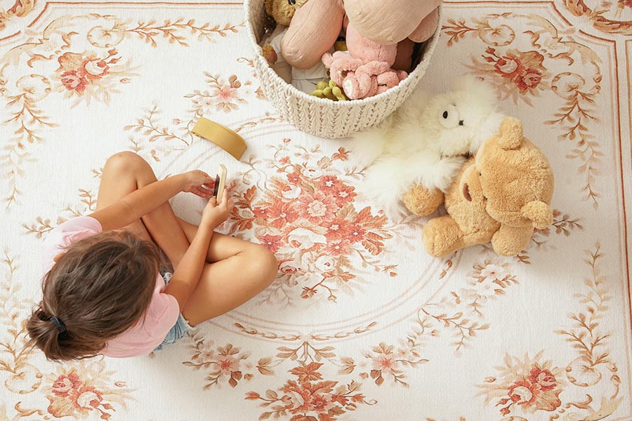 A girl sitting with her toys on a My Magic Carpet washable Aubusson Beige washable rug.