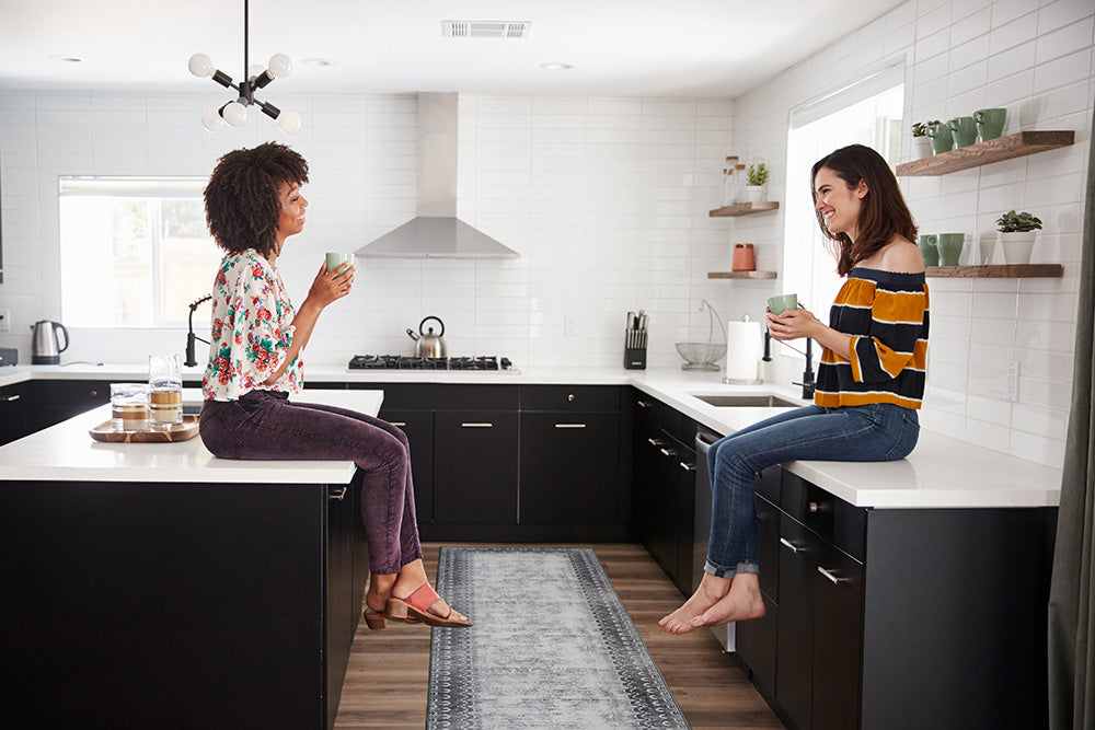 Two women sitting on counters drinking coffee over a runner rug
