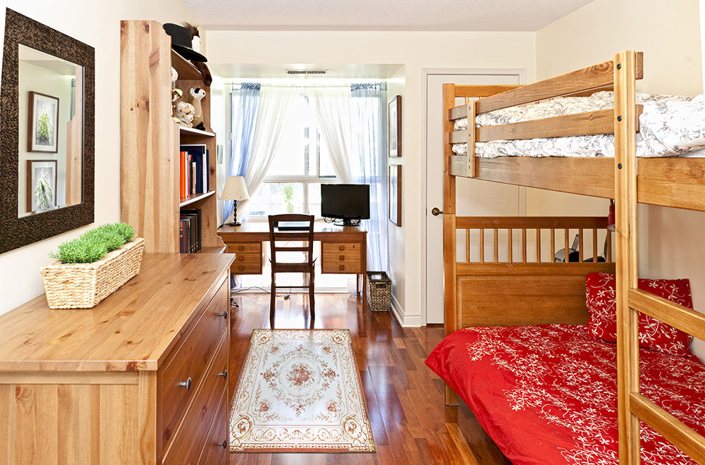 Dorm room with bunk beds a floral rug, dresser, and desk. 