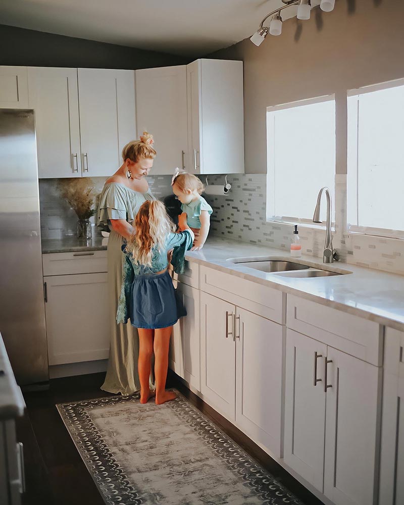 A mom and her kids in a kitchen standing on My Magic Carpet's Dardon Bordered Grey washable rug.