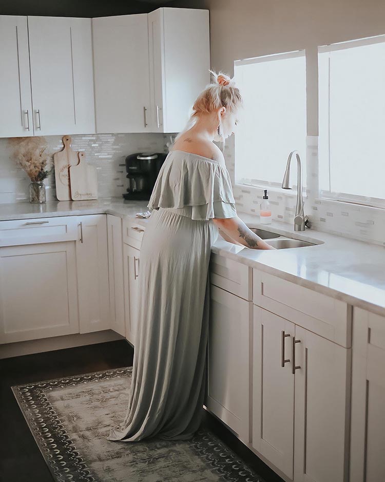 A lady standing on the My Magic Carpet Dardon Bordered Grey washable rug in a kitchen 