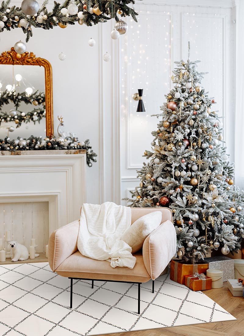 A white living room with a baroque mirror, fireplace, armchair, a flocked Christmas tree and a My Magic Carpet Medina Moroccan Diamond Ivory washable rug.