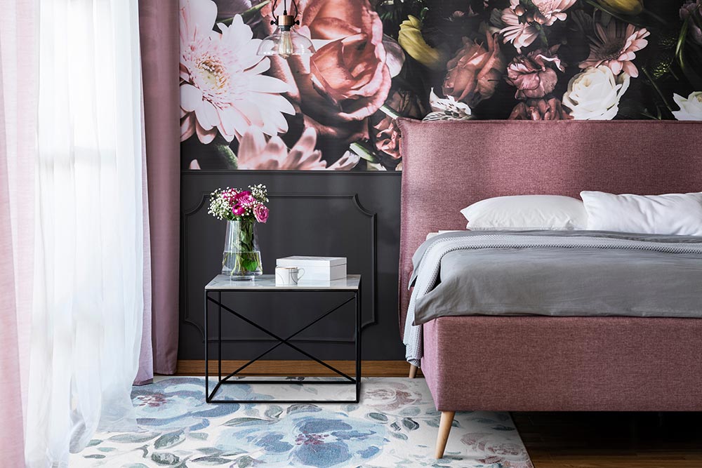 A floral pick hued bedroom next to a window with the My Magic Carpet Sasha Floral Cream Blue washable rug positioned by the bed and night table