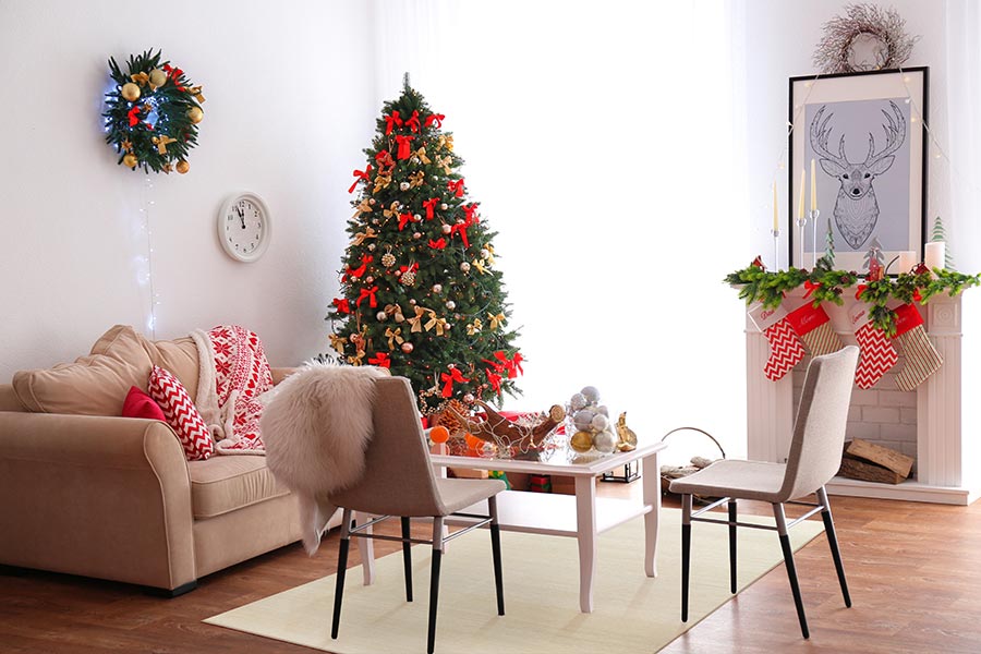 A living room with a couch, table, large window, wreath on the wall, Christmas tree with bows, a mantle with stockings, a picture of a deer and a My Magic Carpet Washable Rug in Solid Cream. 