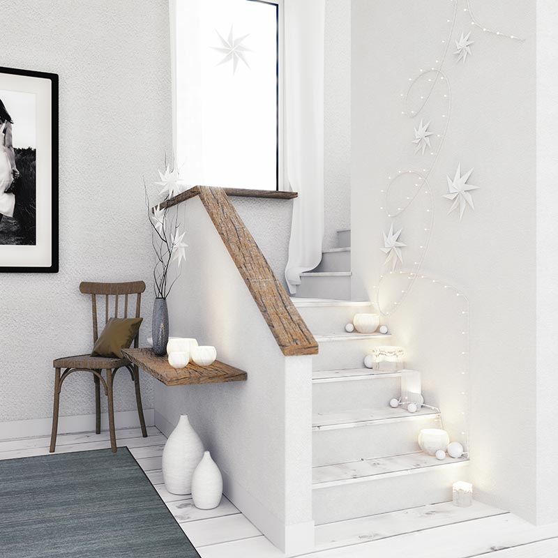 A white staircase with decorative white holiday lights, a neutral hued handrail and a My Magic Carpet Solid Grey Washable Rug.