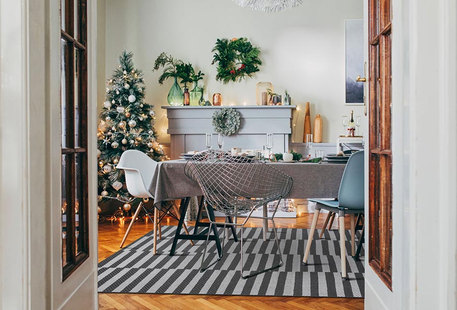 A dining room with a Christmas tree, a wreath, a mantle, a table with mismatched chairs and a My Magic Carpet Tratti Offset Stripe Blue Washable Rug 
