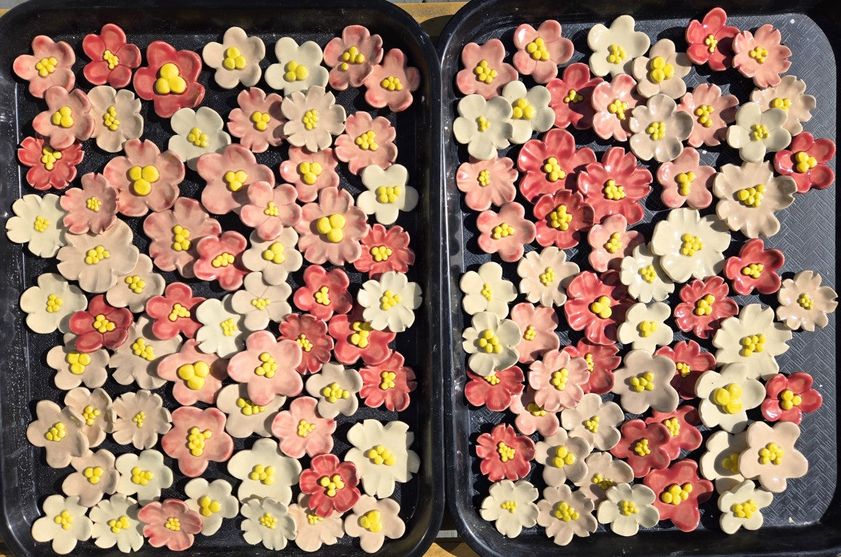 Two black plastic trays hold over a hundred pottery flowers in various shades of pink.