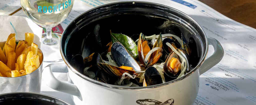 Cooked mussels in a bowl on the dining table at Rockfish with a glass of wine and French fries on the side