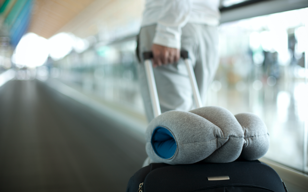 Person carrying luggage with Original Napping Pillow by Ostrichpillow 