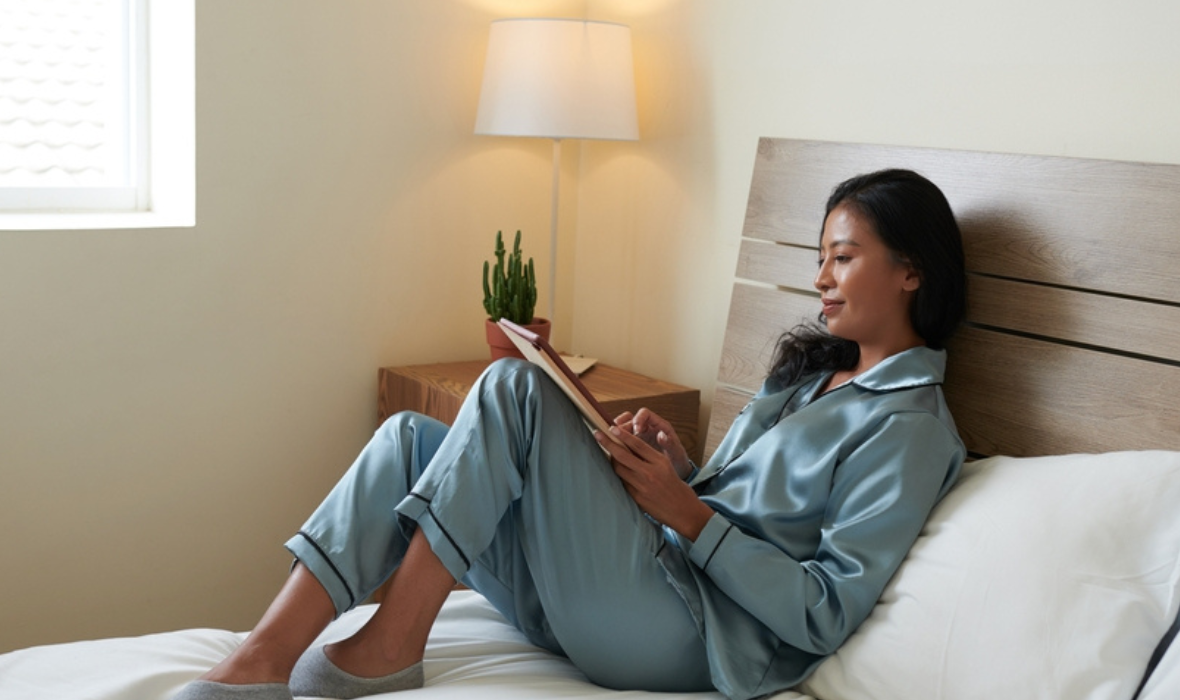 Femme en pyjama sur son lit qui lis un livre