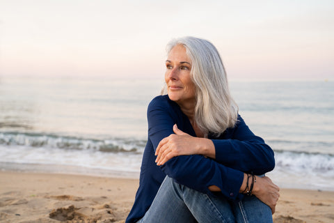 Grey haired Mature woman sitting on the beach  Her skin is glowing in the sunlight