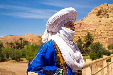 Fehérturbános, kékruhás arab férfi egy oázis szélén a sivatagban