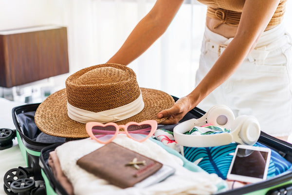 Gros plan sur l'emballage d'une caisse pour les vacances. Il y a un chapeau de paille visible, des lunettes de soleil roses en forme de cœur, un téléphone portable et des vêtements.