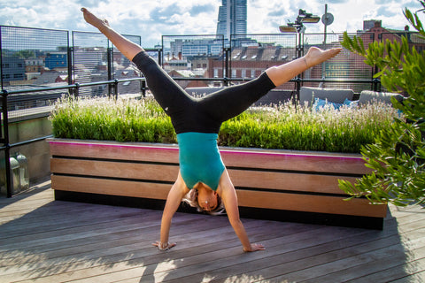 Sarah is doing a handstand with her legs in the splits. She is wearing a Comfizz teal support vest & black sports leggings