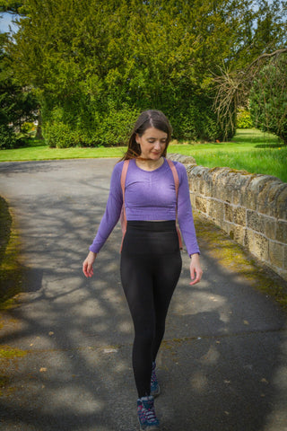 Amy is walking in the countryside, wearing a purple long sleeve crop top, black comfizz leggings and walking boots