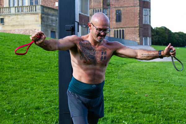 Gareth outside in Temple Newsam Park near Leeds, using resistance bands to exercise, and wearing our pine level 2 support wear and his black shorts.