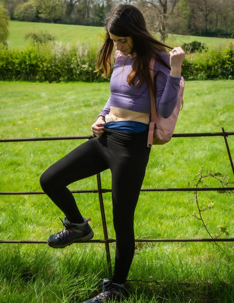 Amy porte nos leggings Comfizz niveau 1 et est appuyée contre une clôture en fer dans la campagne, regardant le haut des leggings.