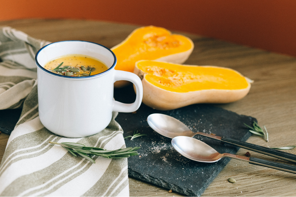 Une tasse blanche de soupe de carottes et de courge musquée, photo avec une courge musquée coupée en deux et 2 cuillères