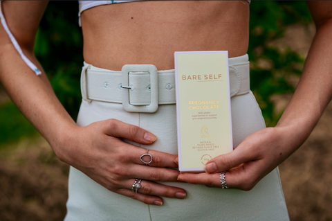 pregnant women holding her belly and pregnancy chocolate in her other hand. 