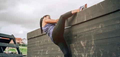 lady climbing a wall obstacle with one leg over the wall