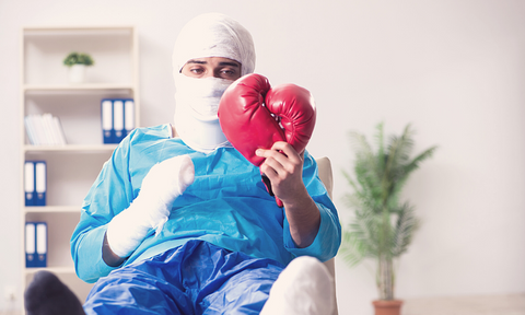 Heavily bandaged injured man looking at his boxing gloves wishing when he can go back to training