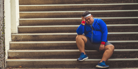 overweight man seated on the stairs tired and frustrated with not progressing with his training