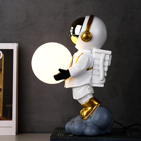 Astronaut Moon Lamp featuring astronaut in white space suit holding moon in both hands by Allthingscurated.