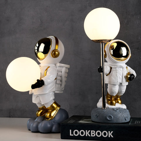 Two astronauts in white space suit. One holding moon in both hands and another holding to a pole with moon attached on top. Astronaut Moon Lamps by Allthingscurated.